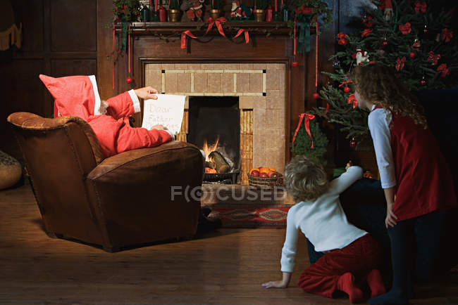Kinder beobachten Weihnachtsmann im Wohnzimmer — Stockfoto