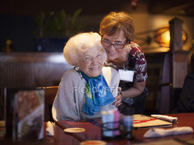 Senior woman sitting at restaurant table, mature woman hugging her — Stock Photo