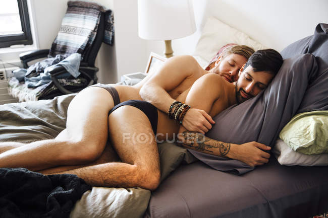 Мужская пара, частично одета, лежит вместе на кровати, спит — стоковое фото