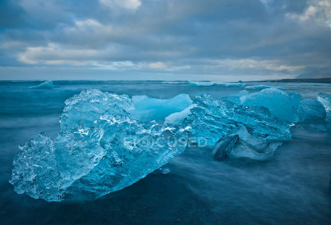 Glaciers washing up on beach under cloudy sky — Stock Photo