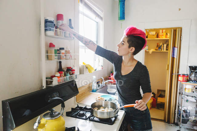 Junge Frau mit pinkfarbenen Haaren bereitet Essen auf Küchenherd zu — Stockfoto