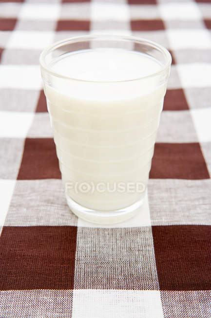 Bicchiere pieno di latte sulla tovaglia a scacchi — Foto stock