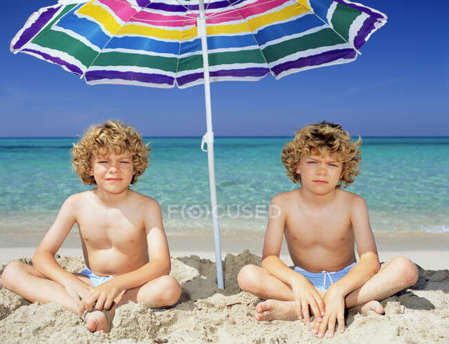 Zwillingsjungen unter einem Sonnenschirm — Stockfoto