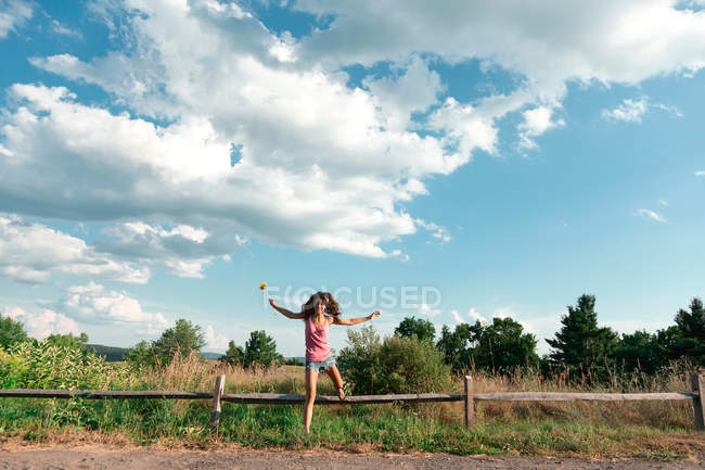 Teenage girl jumping off wooden fence — Stock Photo