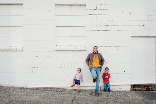 Hombre adulto medio e hijo e hija apoyados contra la pared, retrato - foto de stock
