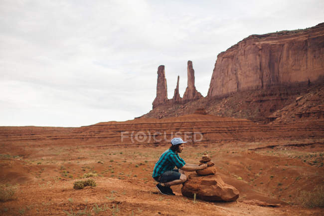 Giovane uomo accovacciato per guardare rocce impilate, Monument Valley, Arizona, USA — Foto stock