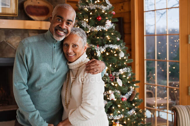 Ältere Paare umarmen sich am Weihnachtsbaum, Porträt — Stockfoto
