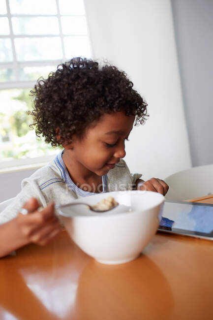 Мальчик завтракает и использует цифровой планшет — стоковое фото