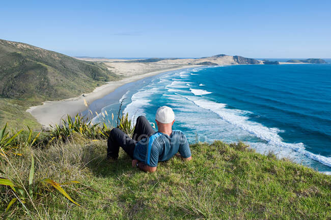 Northland, Kap Reigna, Mann auf Gras liegend, Blick zum Strand — Stockfoto