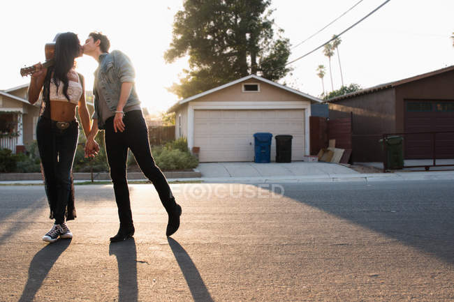 Молода пара цілується на відкритому повітрі, молода жінка тримає гітару — стокове фото