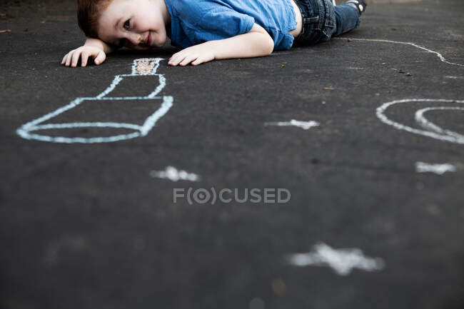 Niño acostado en el suelo mirando tiza dibujo - foto de stock