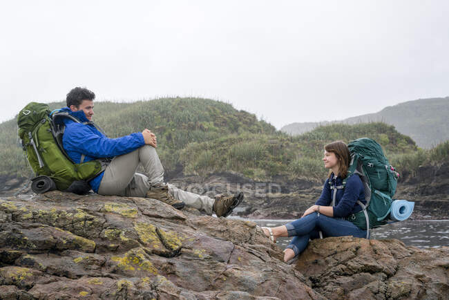 Молода пара з рюкзаком сидить на скелі, Констант Бей, Чарлстон, Південний острів, Нова Зеландія. — стокове фото