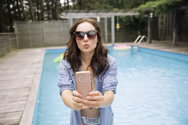 Mujer tomando selfie con teléfono móvil al lado de la piscina, Amagansett, Nueva York, EE.UU. - foto de stock