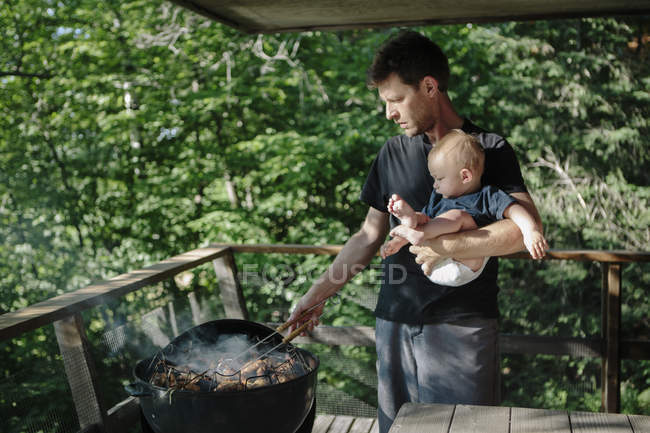Padre sosteniendo a su hijo pequeño mientras convierte la comida en barbacoa - foto de stock