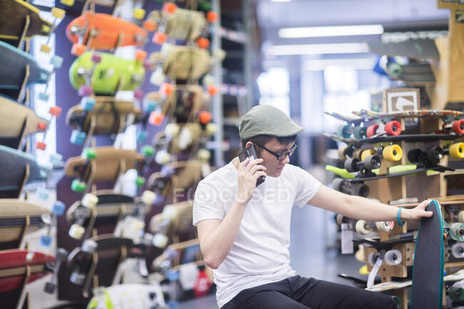 Молодой скейтбордист звонит на смартфон в магазин скейтбордов — стоковое фото