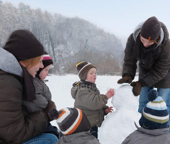 Mujeres y niños construyendo muñeco de nieve - foto de stock