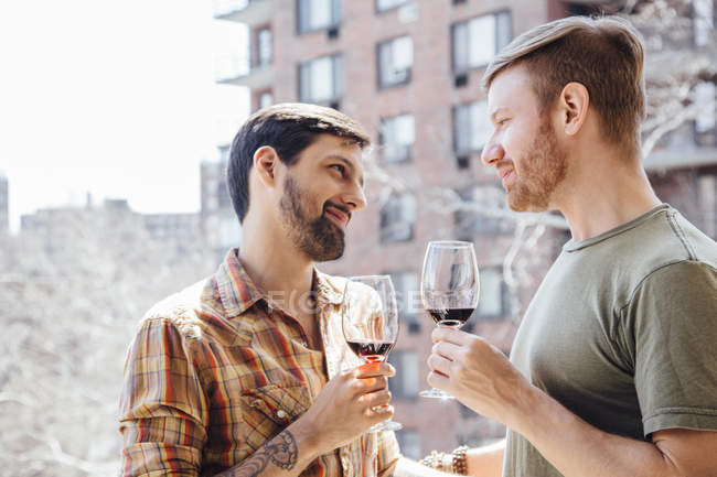 Male couple standing on balcony, holding wine glasses, face to face — Stock Photo