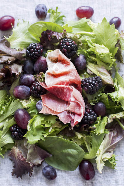 Green salad with grapes, berries and prosciutto — Stock Photo