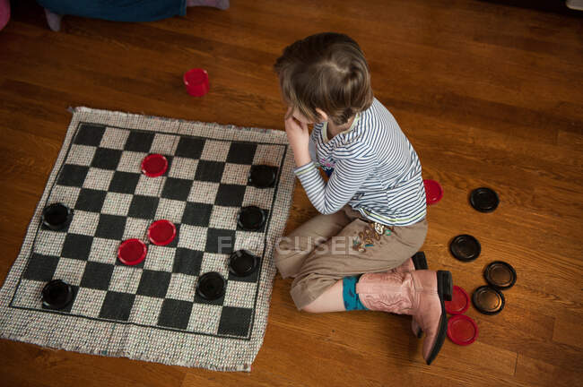 Девушка сидит на деревянном полу и играет в шашки — стоковое фото