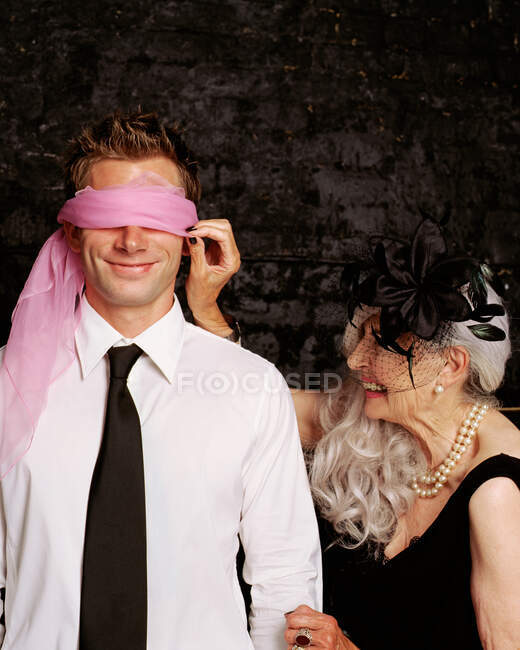Senior adult woman adjusting scarf covering young adult man's eyes — Stock Photo