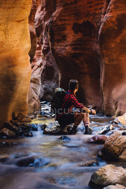 Randonneur assis dans une grotte sur un rocher fluvial, Parc National de Zion, Utah, USA — Photo de stock