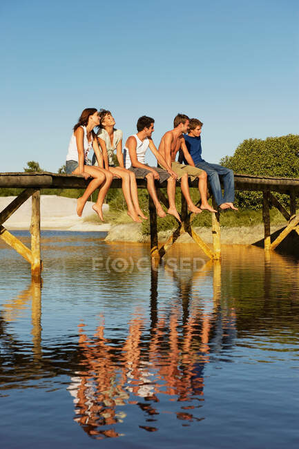 Группа молодых людей, сидящих на пристани — стоковое фото