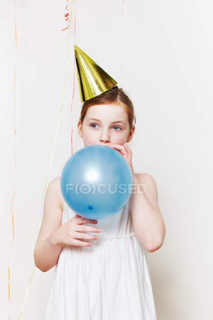 Girl in party hat, blowing up balloon — Stock Photo