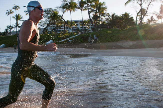 Swimmer running in waves on beach — Stock Photo