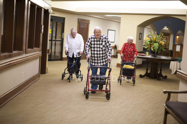 Three senior adults walking indoors with walking frames — Stock Photo