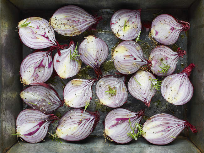 Overhead view of red onion halves with rosemary and olive oil in roasting tin — Stock Photo