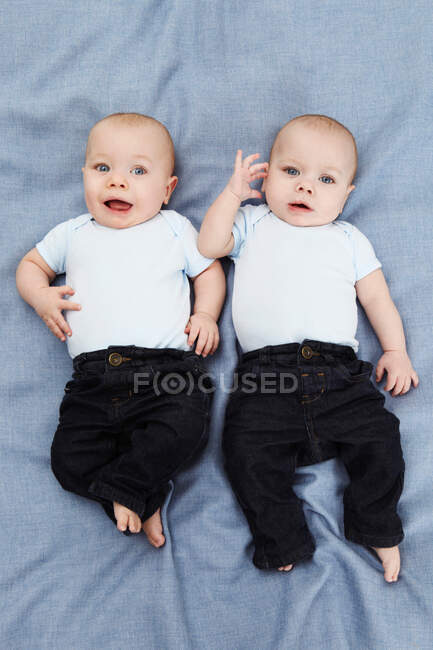 Portrait of two baby boys lying on blue, overhead view — Stock Photo