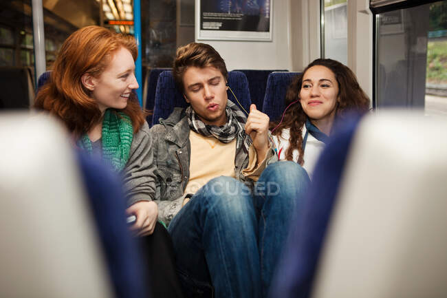 Three young friends travelling on train listening to music — Stock Photo