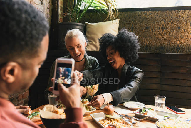 Homem fotografando amigos no restaurante — Fotografia de Stock