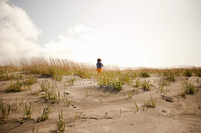 Chico corriendo en dunas de arena - foto de stock