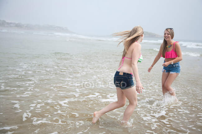 Mujeres jóvenes jugando en la marea en la playa - foto de stock