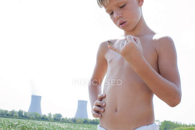 Menino segurando borboleta no dedo mindinho com central nuclear no fundo — Fotografia de Stock