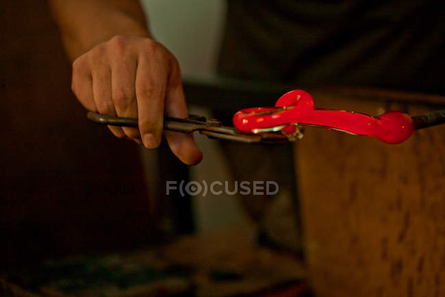 Image recadrée de la personne tenant le verre chaud rouge dans une usine de verre — Photo de stock