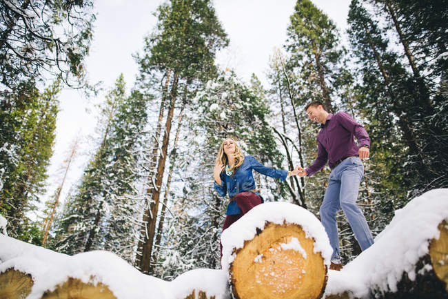 Couple in forest climbing on snow-covered logs — Stock Photo
