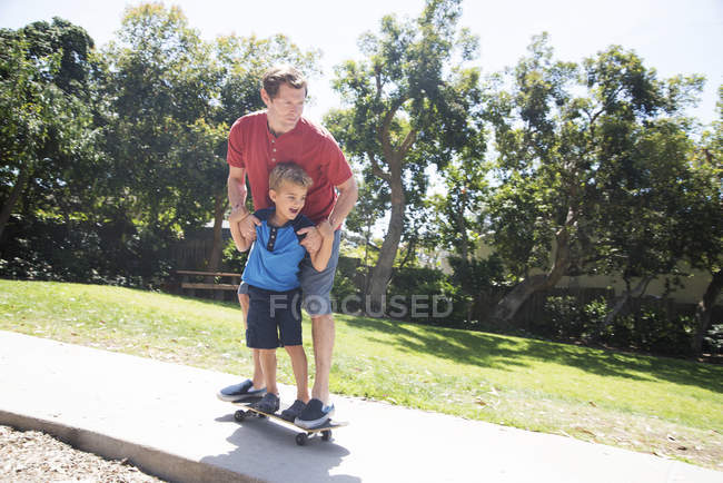 Отец и сын тренируются на скейтборде в парке — стоковое фото