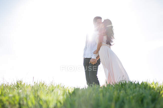 Un couple romantique s'embrasse sur une colline herbeuse éclairée par le soleil — Photo de stock