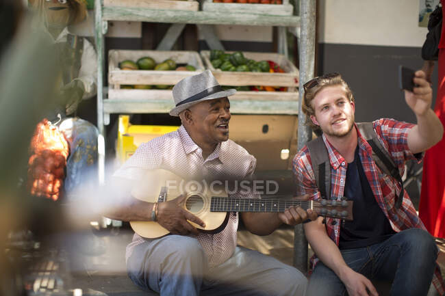 Ciudad del Cabo, Sudáfrica, el hombre tocando la guitarra y la gente en el mercado tomando fotografías - foto de stock