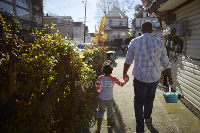 Отец и дочь держатся за руки, идя с ведром — стоковое фото