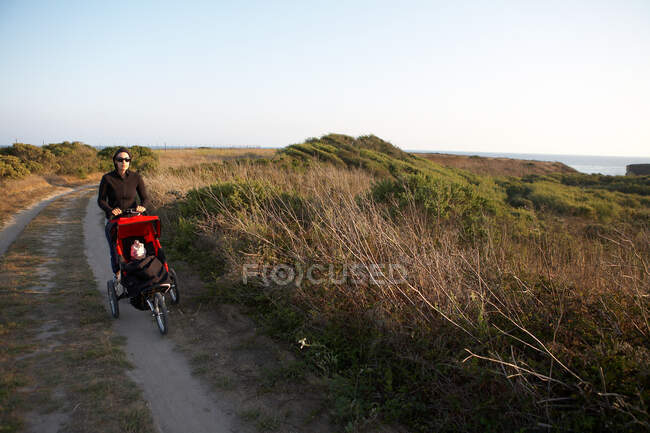 Mother pushing stroller along country path — Stock Photo