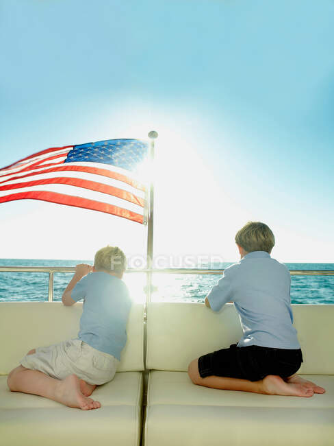 Rapazes na parte de trás de um iate com bandeira americana, a olhar para o mar — Fotografia de Stock