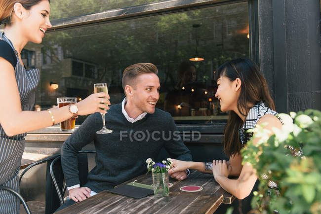 Young couple sitting outside bar, being served drinks by bar worker — Stock Photo