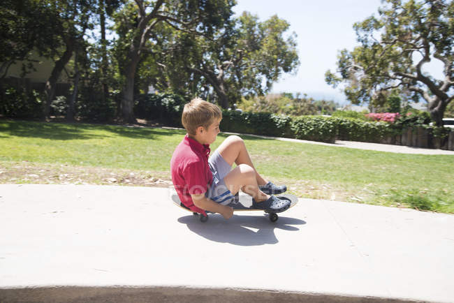 Boy in park skateboarding sitting down — Stock Photo