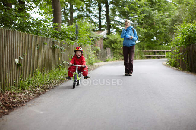 Madre viendo a hijo montar en bicicleta - foto de stock