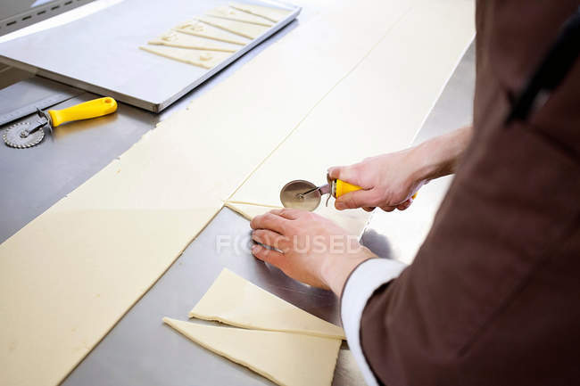 Обрезанный образ Бейкера, разрезающего тесто на кухне — стоковое фото