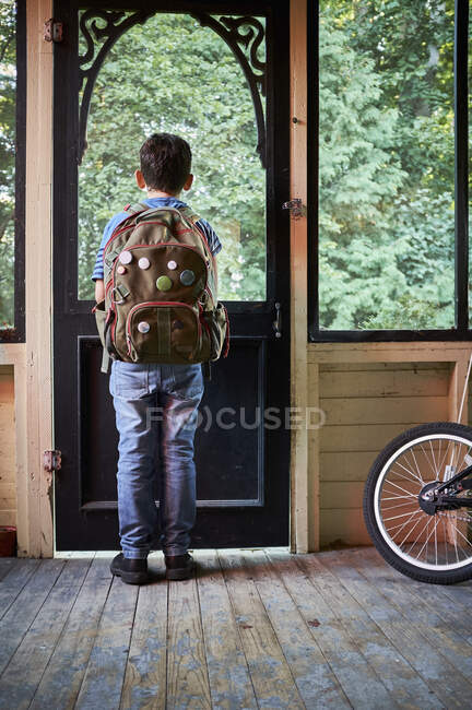 Vue arrière de l'écolier regardant par la fenêtre du porche — Photo de stock