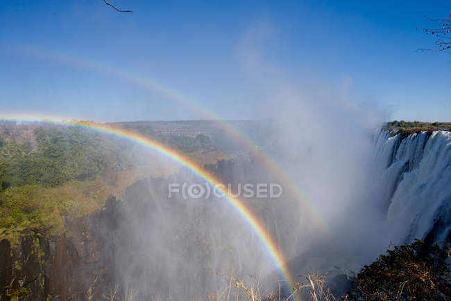 Arco iris en luz solar brillante por encima de las cataratas Victoria - foto de stock